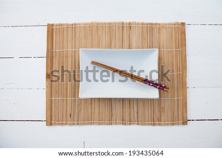 White squared plate with chopsticks and a bamboo table cover on a white wooden table