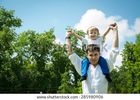 Happy young son on his shoulders at the father against the backdrop of the sky and green forest in summer warm day in the summer