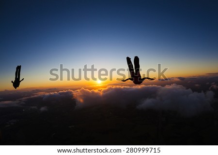 Skydivers silhouette in a beautiful sunset with clouds and blue sky