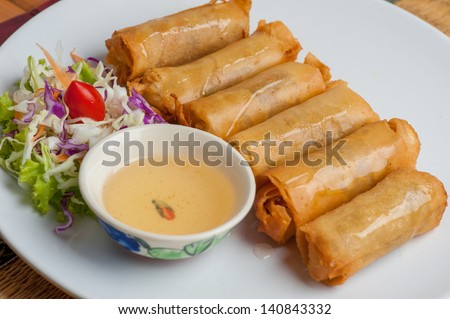 Deep fried spring rolls served with sweet and sour plum sauce on white dish.