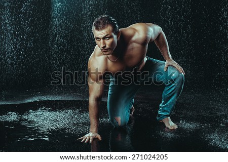 Strong Man Posing Under Rain Drops On Dark Background. Muscular Body. Body-building Model