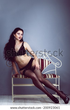 sexy brunette girl sitting on a bench with a forged weary look in erotic black lingerie with stockings with long hair