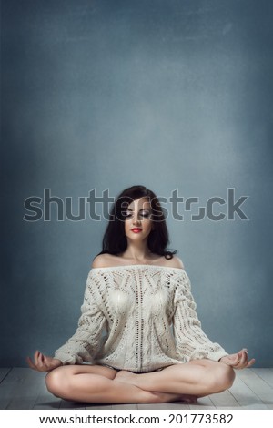 beautiful brunette woman in a lotus position with eyes closed in a sweater sitting cross-legged, with his feet on opposite thighs; used since the times of ancient India