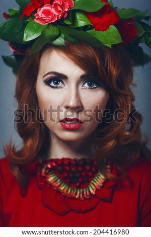 Beautiful sexy red-haired girl in a red dress with makeup and red lips with wreath  with flowers in her hair decoration of flowers around his neck smiling happy smile with teeth