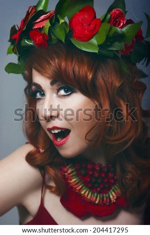 Beautiful sexy red-haired girl in a red dress with makeup and red lips with wreath  with flowers in her hair decoration of flowers around his neck smiling happy
