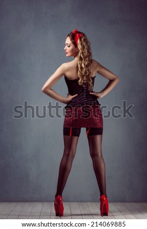 pin up sexy beautiful young blond woman  makeup standing in a corset in a corset and mini skirt black stockings on high heels red shoes