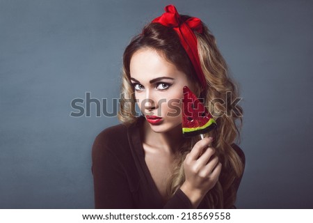 Portrait of beautiful young sexy blonde with a red armband with red lips with a lollipop with watermelon shape sensual temptation to make up pin up