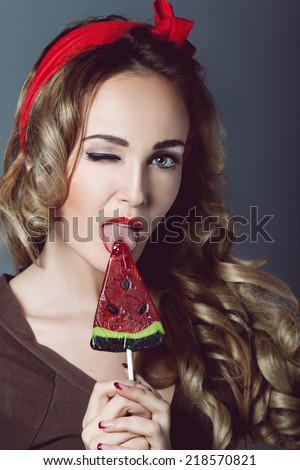 Portrait of beautiful young sexy blonde with a red armband with red lips with lollipop  form watermelon lollipop licking tongue sensual temptation to make up pin up