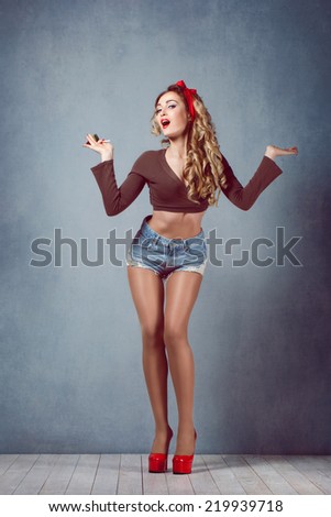 beautiful young sexy blonde slim figure with a red hairband with red lips in denim shorts in red high heels with long legs of sensual temptation emotion surprise delight Pin Up