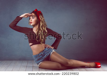 Beautiful young sexy blonde slim figure with a red armband with red lips in denim shorts in red high heels with long legs on the floor sitting  Pin up