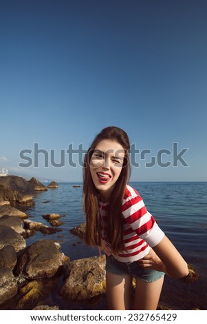 pin up young beautiful girl on the sea in short jeans and striped T-shirt with long hair  gulls water clouds wave dream figure with glasses emotions, smile with teeth, open mouth, red lipstick,