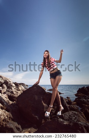 pin up young beautiful girl on the sea in short jeans and striped T-shirt with long hair rocks glasses gulls water clouds, day, wave, dream