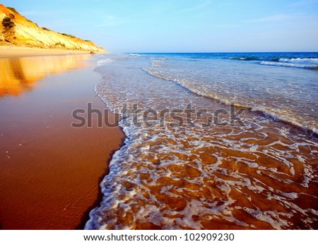 Orange cliffs, tide and sand beach on the Atlantic ocean coast in Algarve(Portugal)