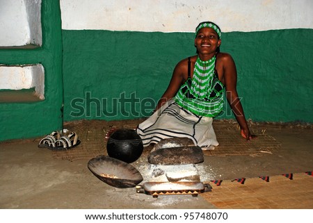 LESEDI CULTURAL VILLAGE,SOUTH AFRICA - JAN 1:Zulu woman in handmade dress cooking maize meal at tribal house on January 1,2008 at Lesedi Village, South Africa.Maize meal is basic Zulu ingredient.