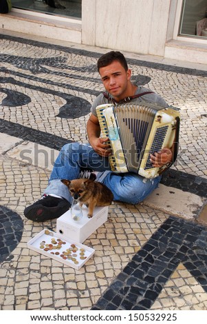 LISBON, PORTUGAL - SEPTEMBER 29 : Young beggar musician with small cute dog play accordion and ask for money on street of Lisbon, Portugal at September 29, 2009.