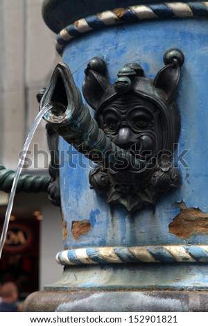Close-up detail of medieval fountain with face blowing shell horns and stream water in Lucerne, Switzerland.