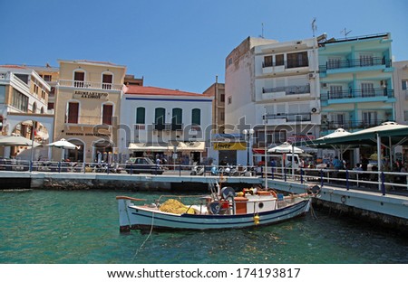 AGIOS NIKOLAOS, GREECE - JULY 18, 2012: Outdoor greek tavern, small shops and fishing boat  in harbor of Agios Nikolaos, Crete, Greece.