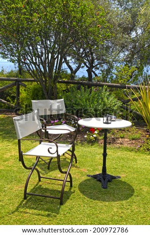 Table and iron chairs on green grass in garden with flowers, trees and sea view(Greece)