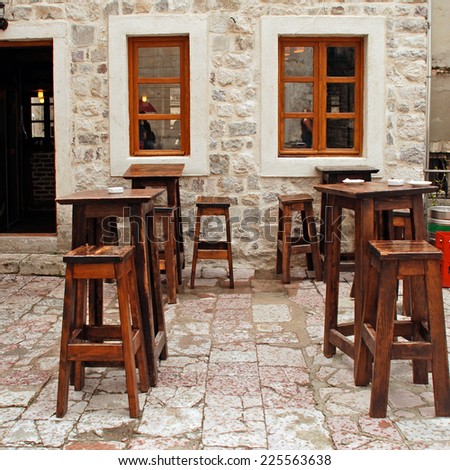 Outdoor cafe with wooden furniture and stone wall at small patio in old european town. Summer rain. Square image