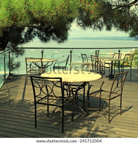 Terrace outdoor cafe with iron chairs, pine trees and sea view in Greece. Square toned image, instagram effect