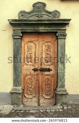 Vintage brown wood medieval door with ornate stone portal in rural stone wall house, Italy