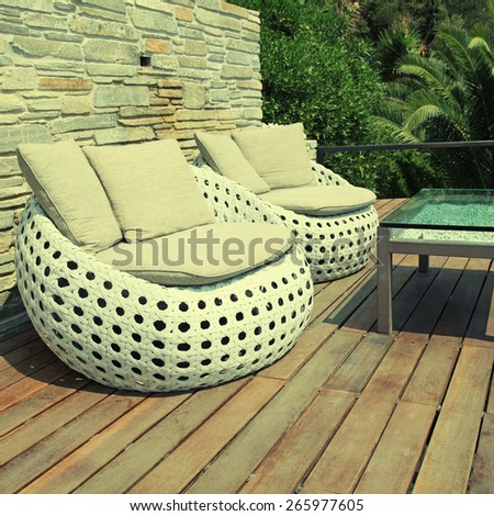 White outdoor furniture round rattan armchairs and glass table on wood resort terrace, Greece. Square toned image, instagram effect