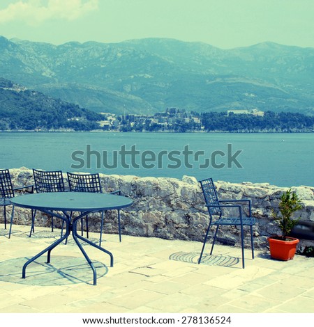 Blue iron chairs and table on beautiful stone terrace in Budva and Adriatic sea (Montenegro). Square toned image