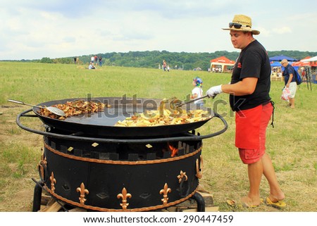 KIEV, UKRAINE - JUNE 21, 2015: Man cooking crisp potato on the huge grill outdoor pan in Museum of Ukrainian Folk Architecture and Rural Life PYROGOVO in Kiev, Ukraine