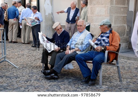 EVORA,PORTUGAL-MAY 03:Old men on bench reading newspapers and discussing news on May 03,2009 in Evora,Portugal. Evora is ranked number two in Portugal most livable cities survey of living conditions.