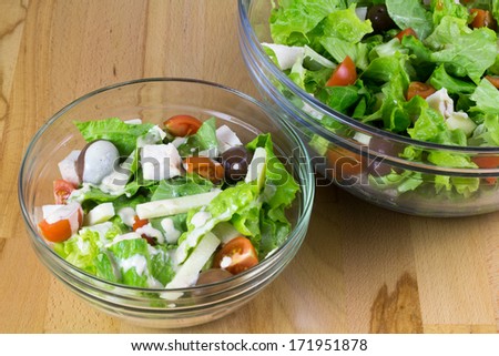 Two bowls of fresh vegetable salad with yellow cheese and chicken meet, served on a wooden table