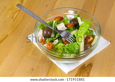 Bowl of fresh vegetable salad with yellow cheese and chicken meet, served on a wooden table
