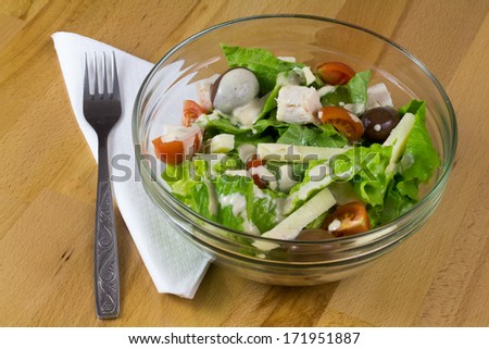 Bowl of fresh vegetable salad with yellow cheese and chicken meet, served on a wooden table