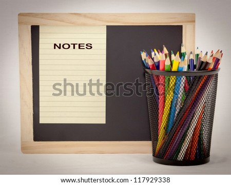 A Chalkboard with  notepad paper and colored pencils in a holder