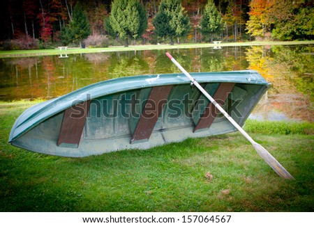 A boat with a paddle on a lake in the  fall season with trees and leaves changing color