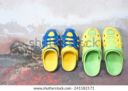 Children\'s colorful sandals rubber old wall concrete background.