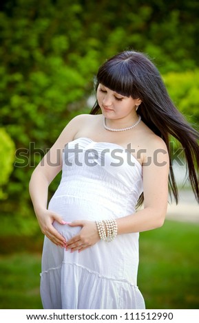 Woman holding her hands in a heart shape on her pregnant belly 	Woman holding her hands in a heart shape on her pregnant belly