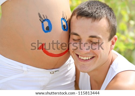 Painted happy smiley face on the belly of pregnant woman