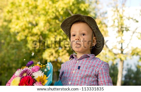 Bemused little boy pulling a funny expression holding a bunch of flowers for his mother on Mothers Day or Valentines with copyspace