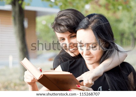 Two young women in a close embrace laughing together at the contents of a book