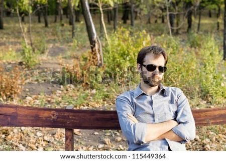 Young bearded man sitting with his arms folded on a rustic wooden bench deep in thought