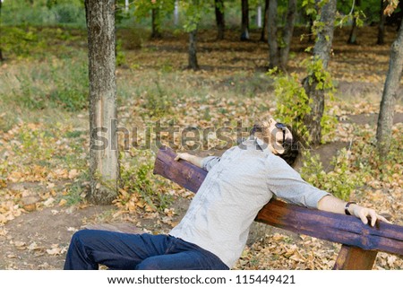 Man enjoying the autumn sunshine sitting on a park bench in woodland with his head thrown back with copyspace