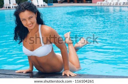 Beautiful smiling woman in a bikini balancing on the edge of a sparkling blue pool