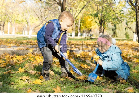 Children digging outdoors with spades in an autumn woodland park with copyspace - stock photo