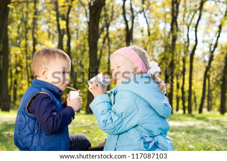Young boy and girl drinking from juices boxes in a park in autumn
