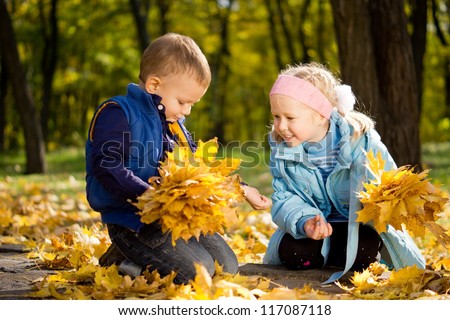 Attractive little brother and sister in autumn woodland kneeling amongst colourful yellow fallen leaves watching an insect on the boys arm with fascination