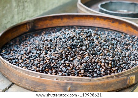 Fresh roasted coffee beans for sale in a flat round container at an outdoor market