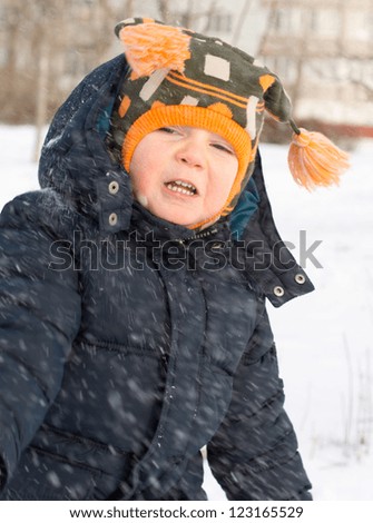 Cute little boy with a warm woolly cap with tassles caught in a flurry of snow drifting down past his face as snowflakes on a freezing winter day