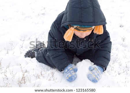Little boy kneeling down gathering up snow in his gloved hands to make a winter snowman or snowballs