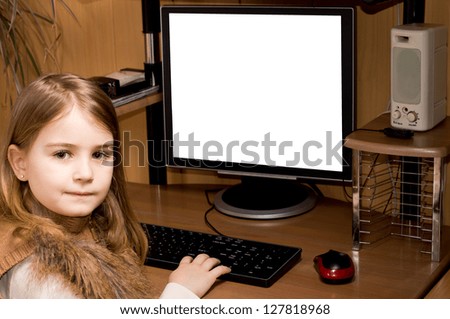 Little girl sitting at a desk in a home office using a desktop computer with a large blank white screen looking back over her shoulder at the camera