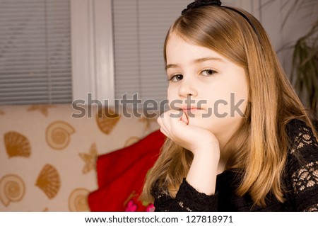 Pretty pensive little girl resting her chin on her hand and glancing sideways at the camera sitting indoors with copyspace